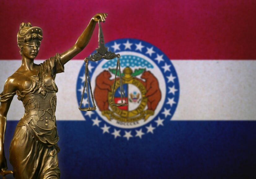 Close-up of a small bronze statuette of Lady Justice before a flag of Missouri.