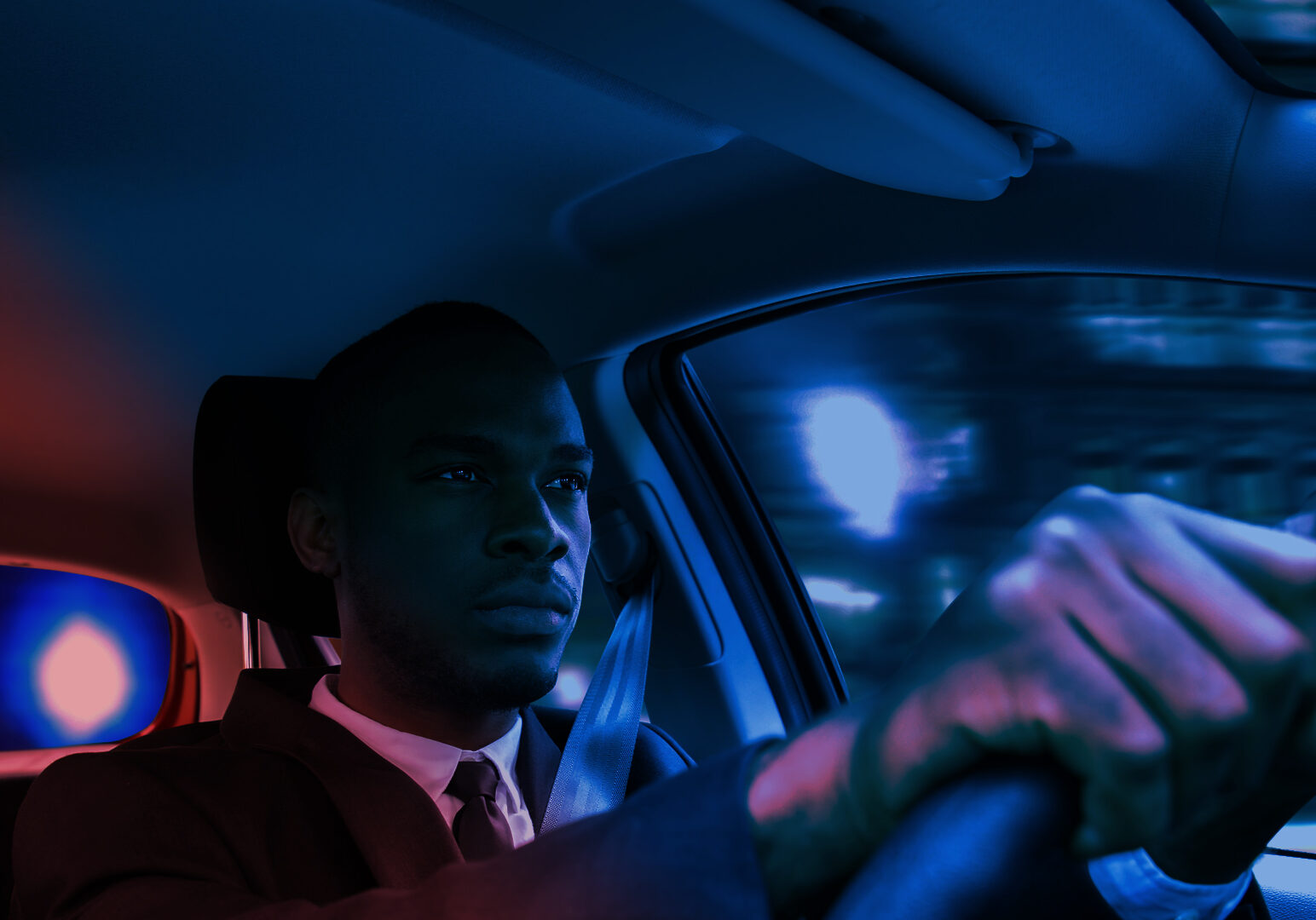Black man behind wheel of automobile, red and blue lights