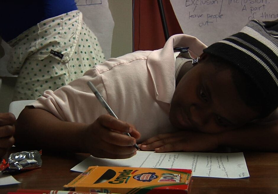 Image of young woman sitting with head down on a desk as she fills out a worksheet.