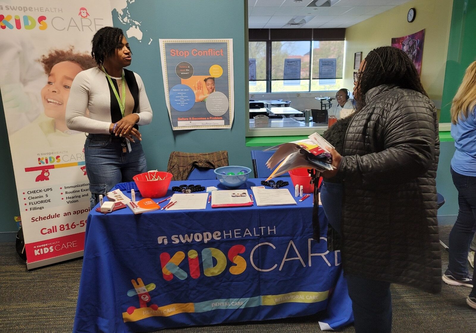 Two people stand by a Kids Care table, covered with a blue cloth for Swope Health