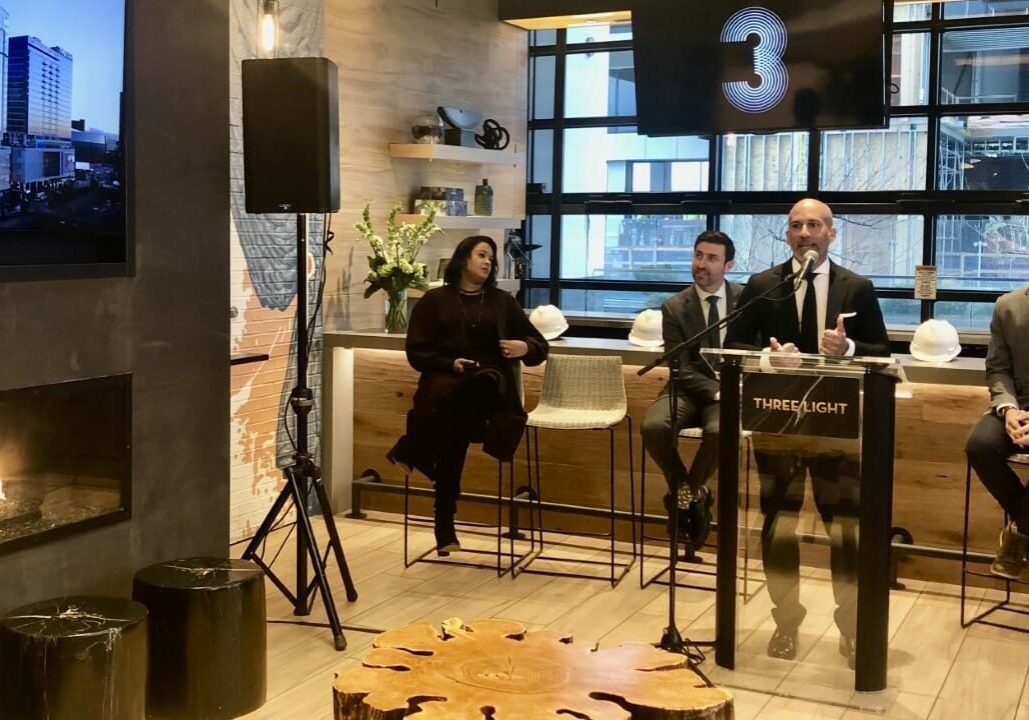 John Moncke, president of the Power & Light District, speaks at the Three Light topping-off event, City Manager Brian Platt is seated to his left, City Councilman Eric Bunch to his right.