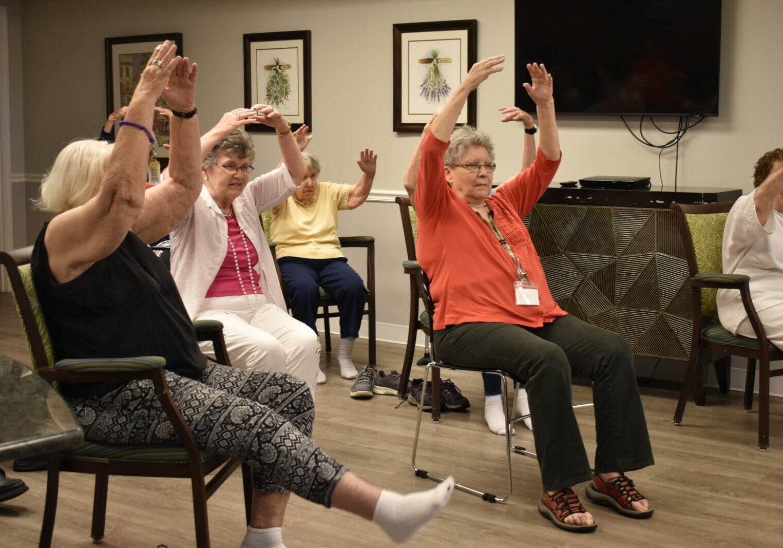 A group of older women hold their arms up in fifth position while seated.