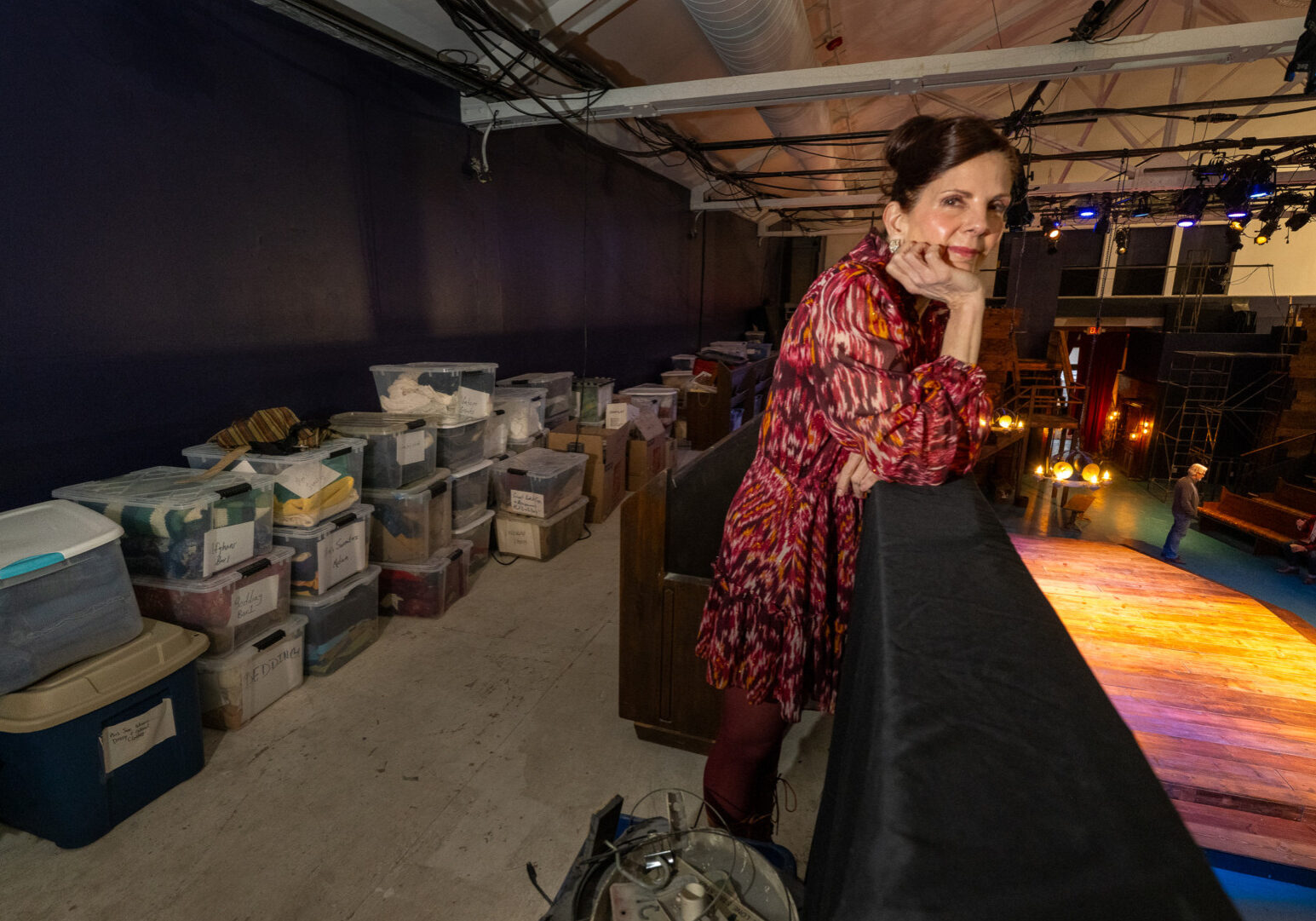 Karen Paisley, artistic director and cofounder of the Metropolitan Ensemble Theatre, stands in a balcony above the stage at the Warwick Theatre. Behind her are storage tubs full of costumes that she and volunteers cleaned after a devastating fire at the site two years ago, on Feb. 6, 2024. (Todd Feeback | Flatland)