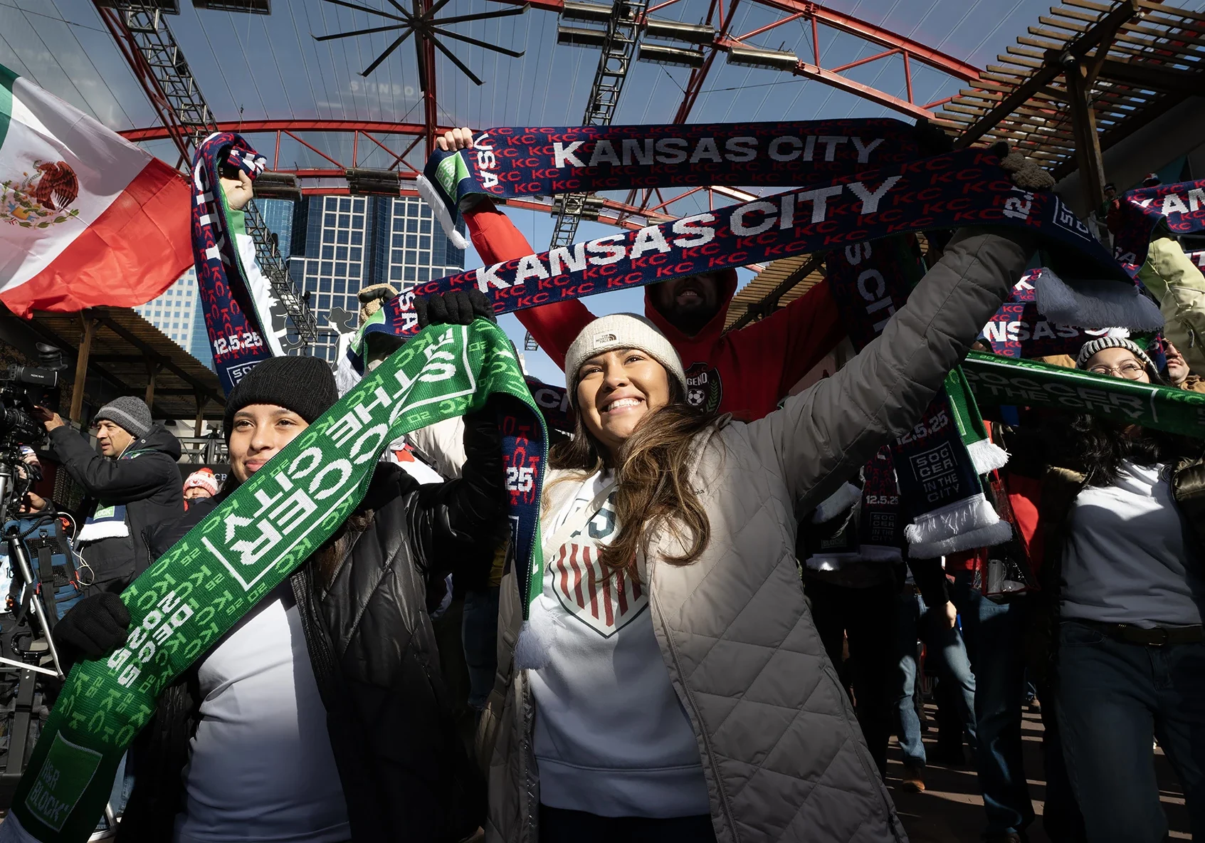 Scarves aloft, Ali Samaniego, at left, and Veronica Brewer celebrate at a regionwide watch party for the final draw. In the countdown to the FIFA World Cup, the event drew a crowd Friday morning to KC Live! in the Power & Light District. (Julie Denesha | KCUR 89.3)