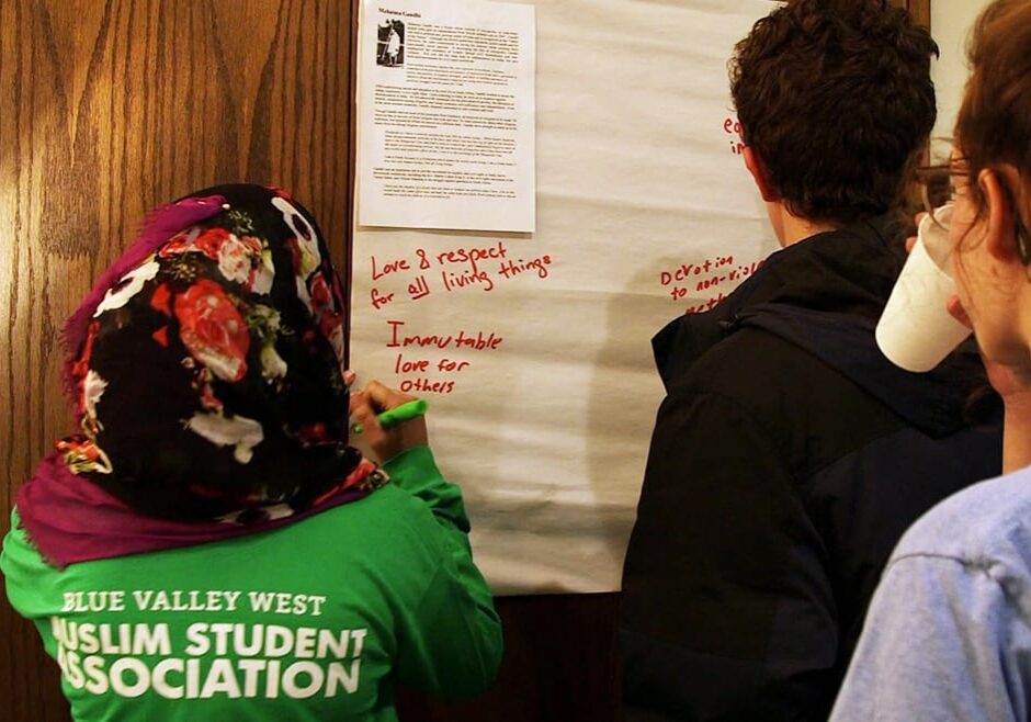 Young woman in green shirt writes on paper.
